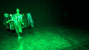 A green light shines on Kim Miller doing a performance artwork