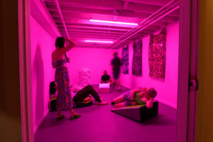 People lay and stand in a space lit with bright pink light