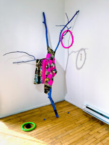 An abstract sculpture of a stick draped in colorful objects