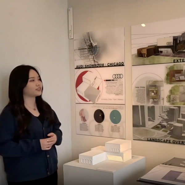 A student stands in front of her senior exhibition display of an Audi dealership showroom design