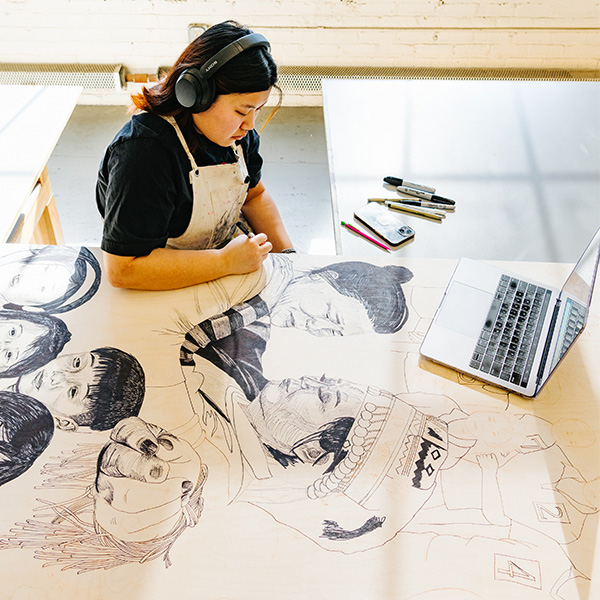 Adm_HowtoApply_Transcripts A student sits at a desk working on a large woodcut print.