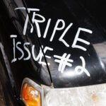 "Triple Issue #2" is written in white on the front hood of a black car.