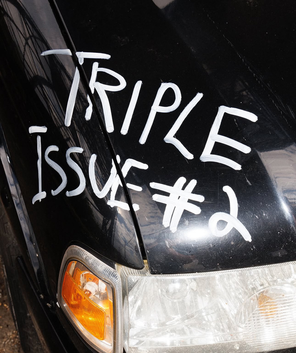 "Triple Issue #2" is written in white on the front hood of a black car.