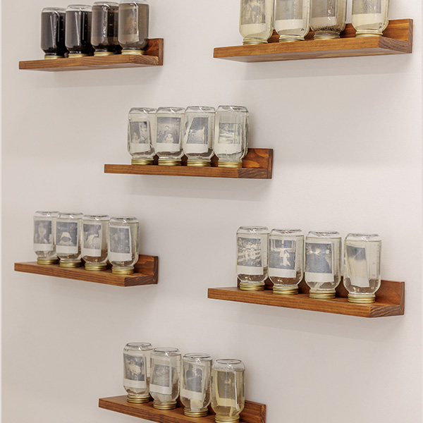 Floating shelves hold upside-down Mason jars filled with liquid and polaroid photos.