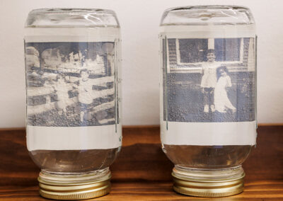 Two mason jars filled with liquid, each containing one polaroid photo of children.