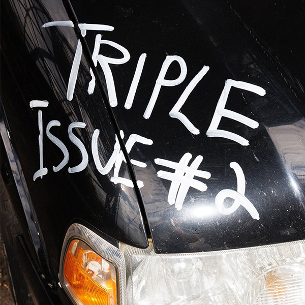 "Triple Issue #2" is written in white on the front hood of a black car.