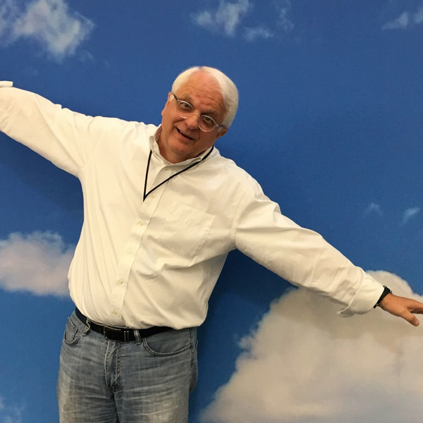 A photo of a man holding his arms outstretched like a plane against a blue sky with clouds