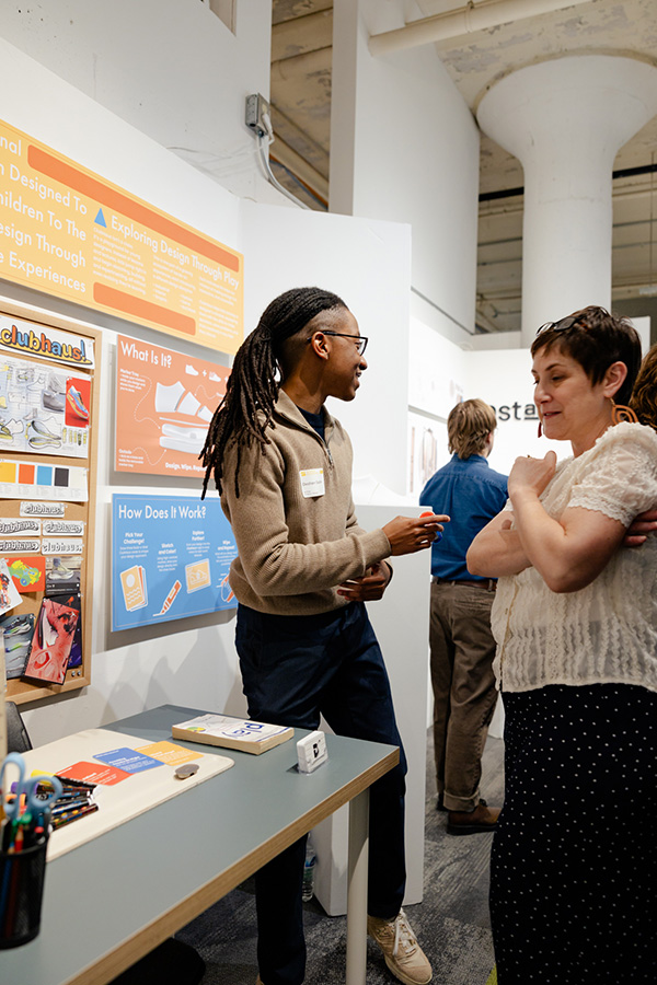 AlumniSeniorThesisAwards_DesharrSaddler Desharr Saddler talks to a visitor during the 2025 Senior Exhibition.