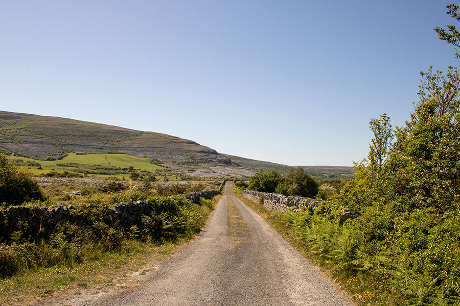 A photo of a gravel road bordered by a stone wall in Ballyvaughan, Ireland.