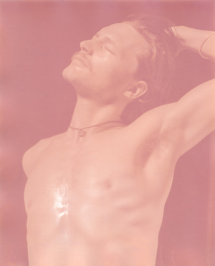 A pink-tinged photo of a shirtless person with their eyes closed.