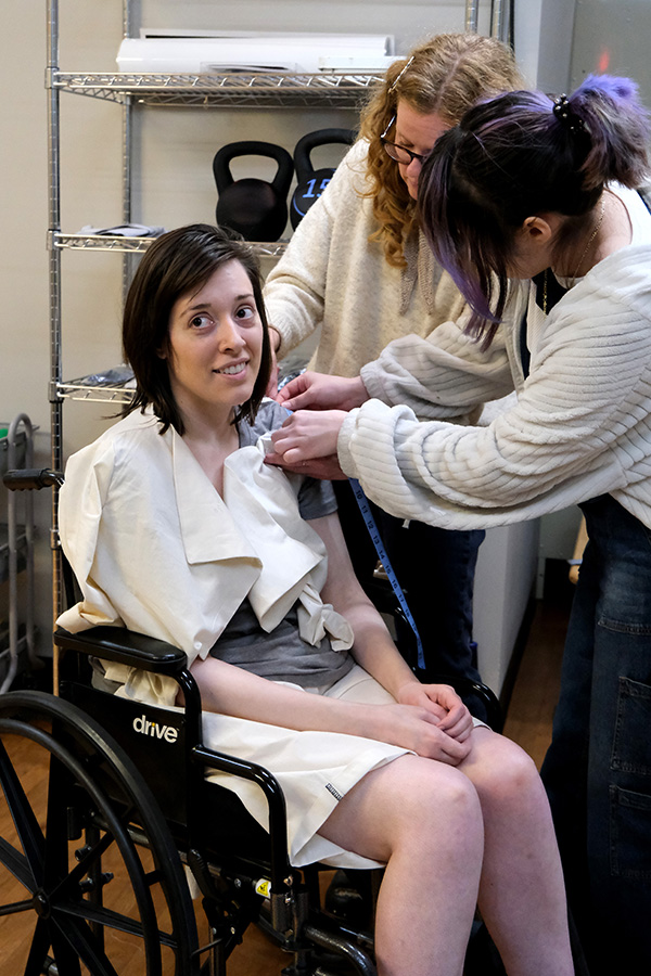 Andrea Gonzalez smiles while a MIAD student and instructor adjust the fit of a garment.