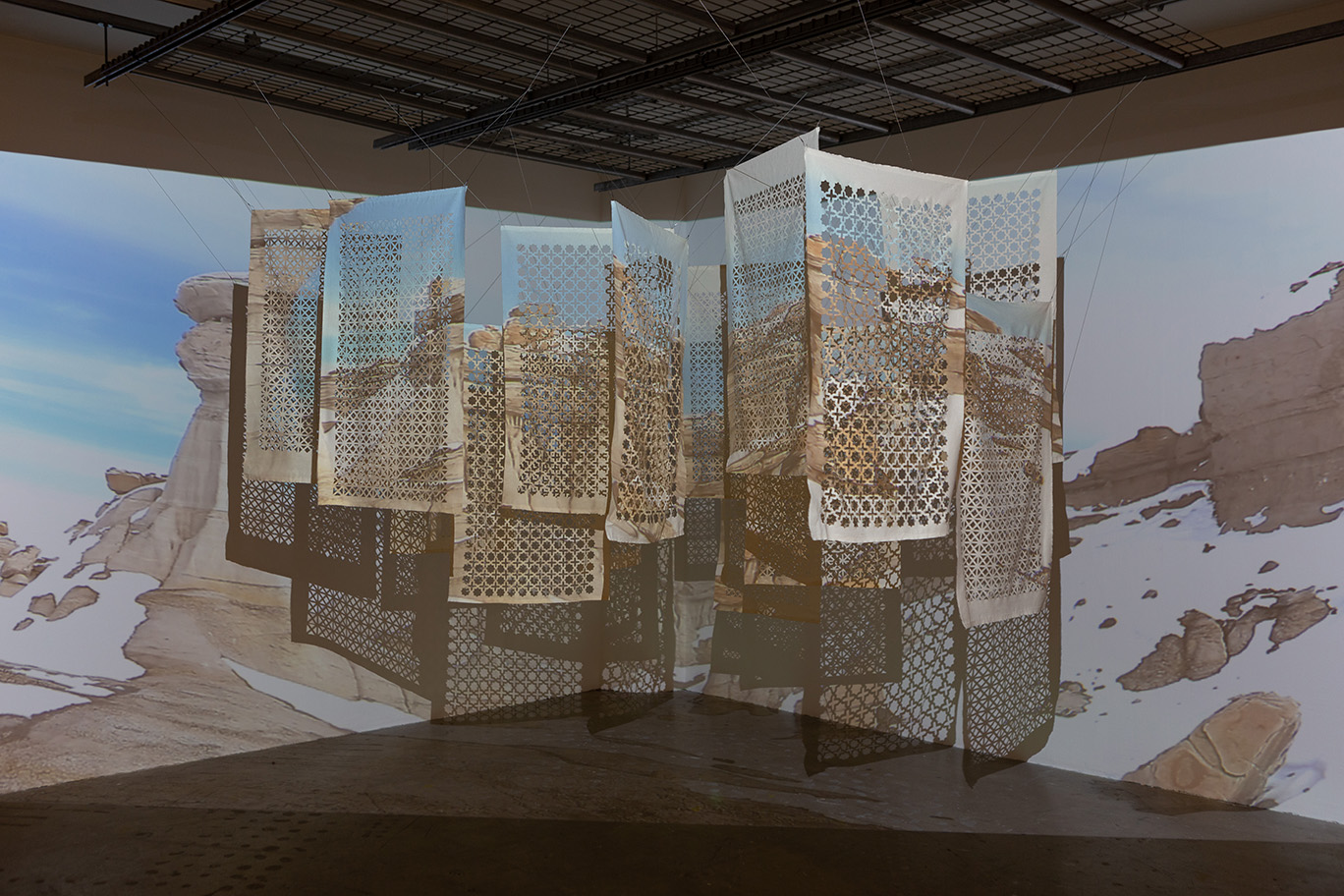 An installation of fabric rectangles hanging from the ceiling with a mountain image projected onto them