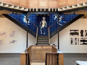 A blue installation with white human figures on the wall framed by a staircase.