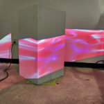 An abstract pink projection is projected sideways onto a neutral gray block.