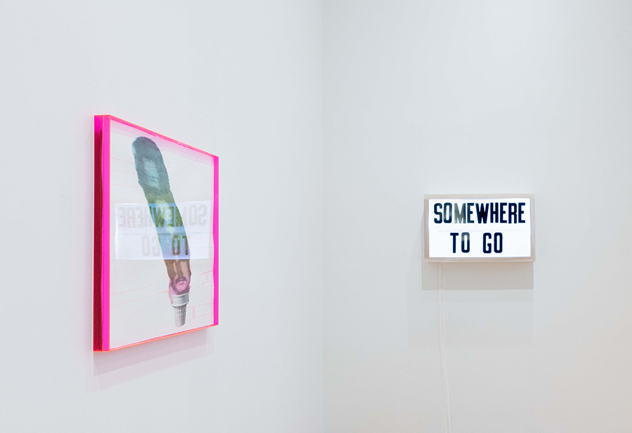 A white-walled corner with a pink-framed artwork and a box that says "Somewhere to Go"