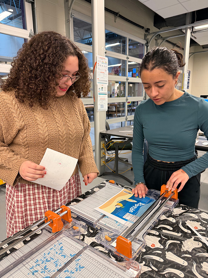 Two high school students use a paper cutter.