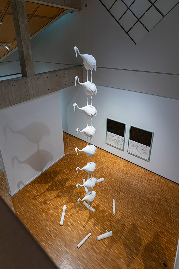 A column of white sculptures of cranes extends to the ceiling of a museum