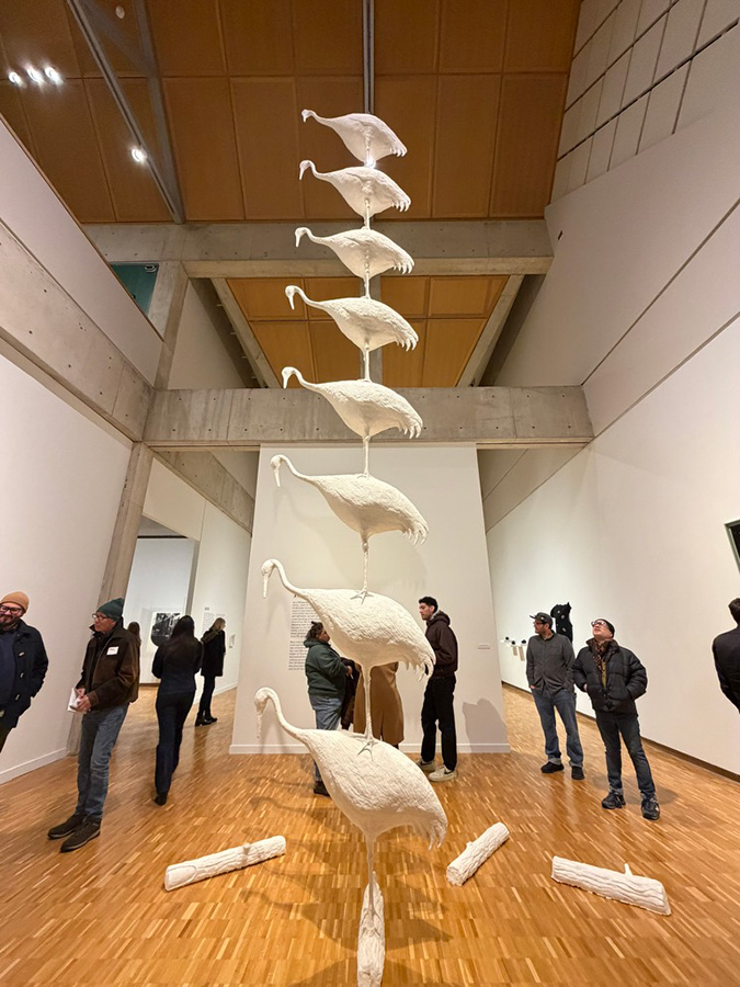 People look at a tall column of sculptural cranes installed in a museum