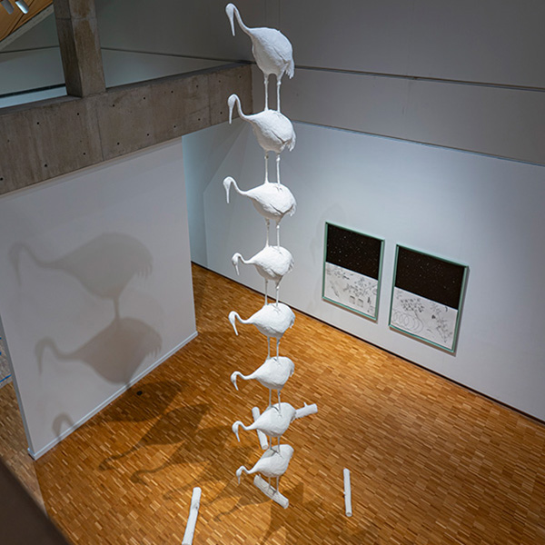 A column of white sculptures of cranes extends to the ceiling of a museum