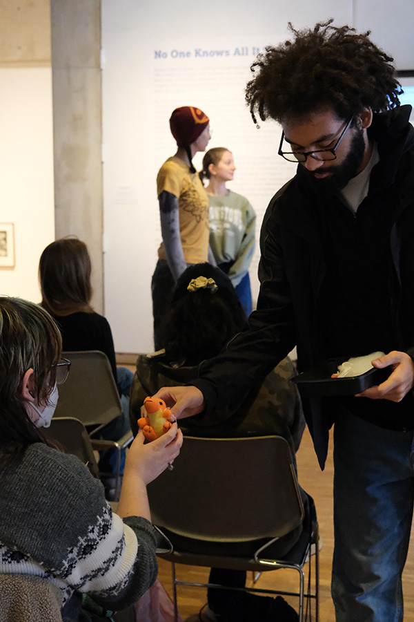 A student hands a small orange stuffed animal to an audience member.