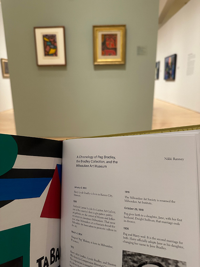 A catalog program open to a page that credits Nikki Ranney; the exhibition artwork is in the background