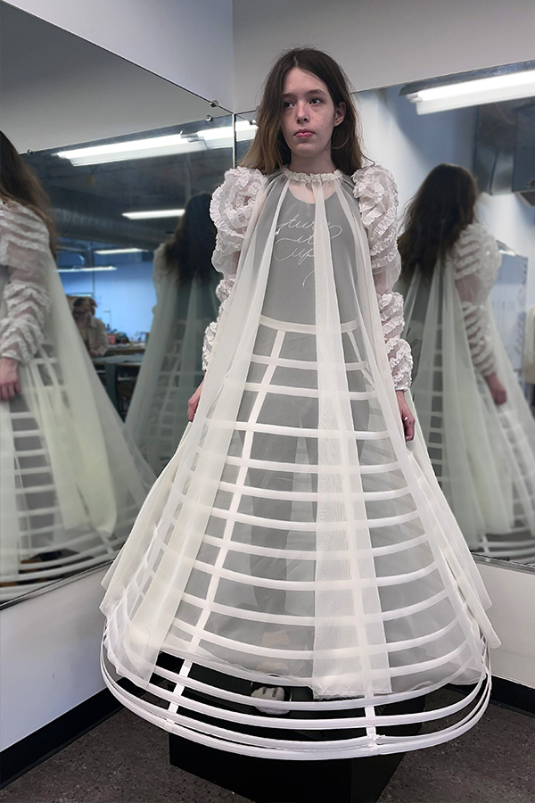 A woman wearing a skeletal form covered in sheer fabric poses in front of two mirrors