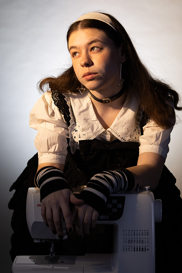 A young woman leans over a sewing machine in golden light