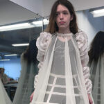 A woman wearing a skeletal form covered in sheer fabric poses in front of two mirrors