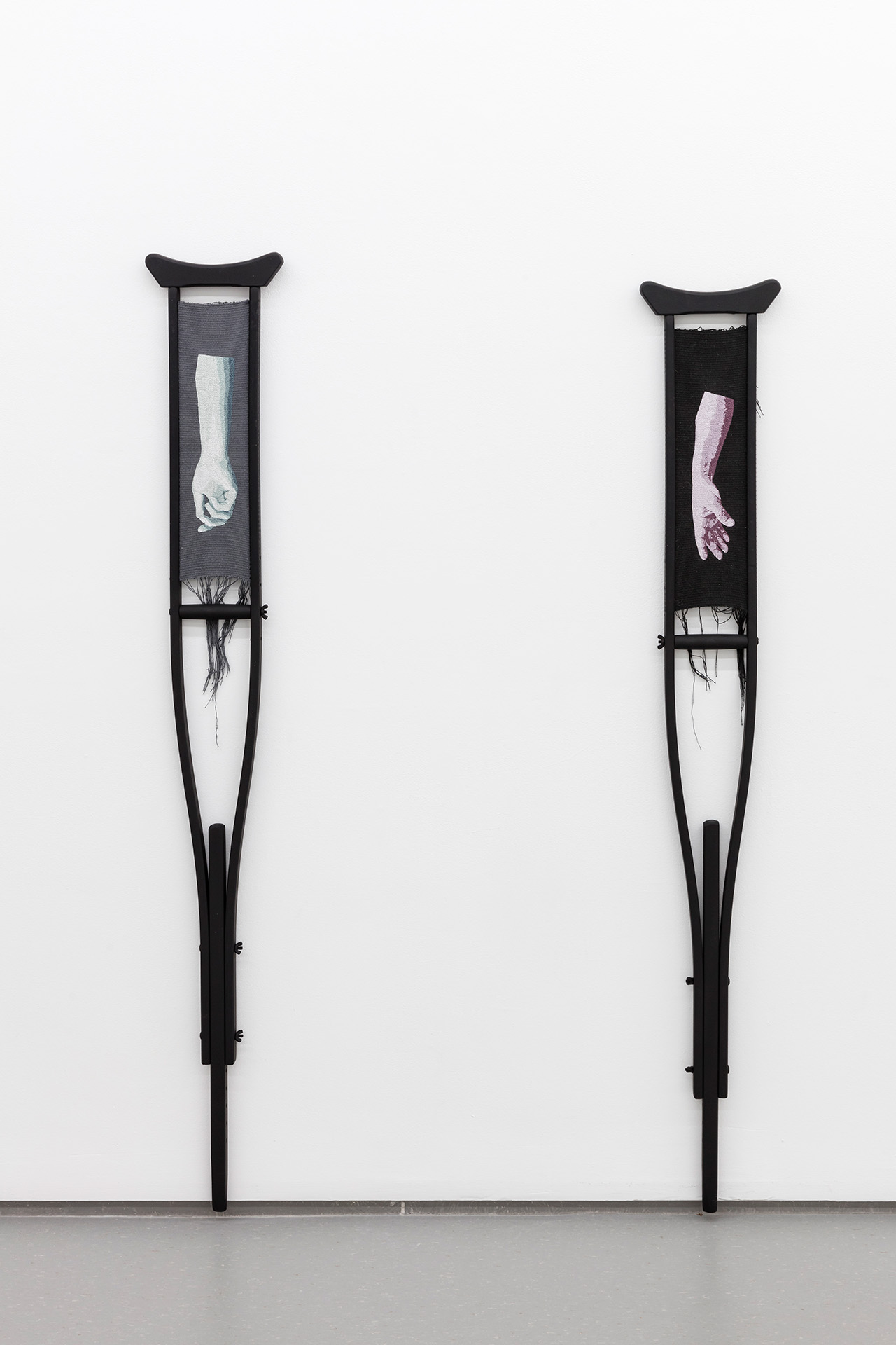 Two black wooden crutches with hand woven embroidery of images of arms