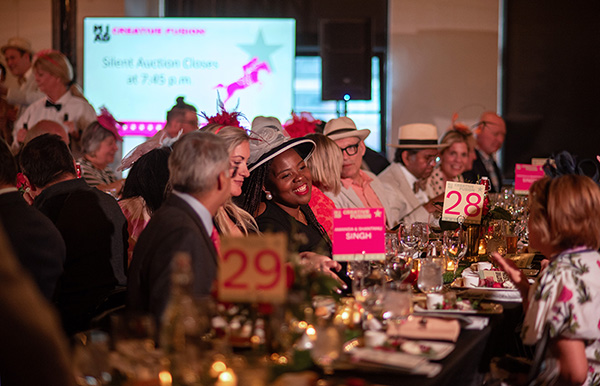 a large group of people sitting at a table dining and smiling during an auction