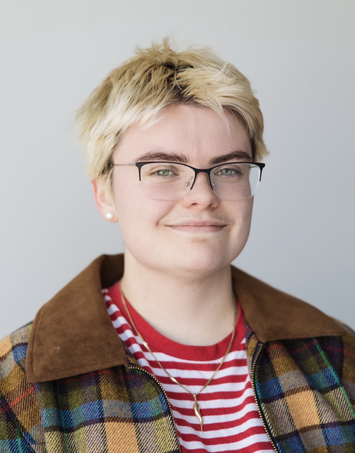 Portrait of a Brooke Thompson with short blond hair wearing glasses and a plaid jacket.