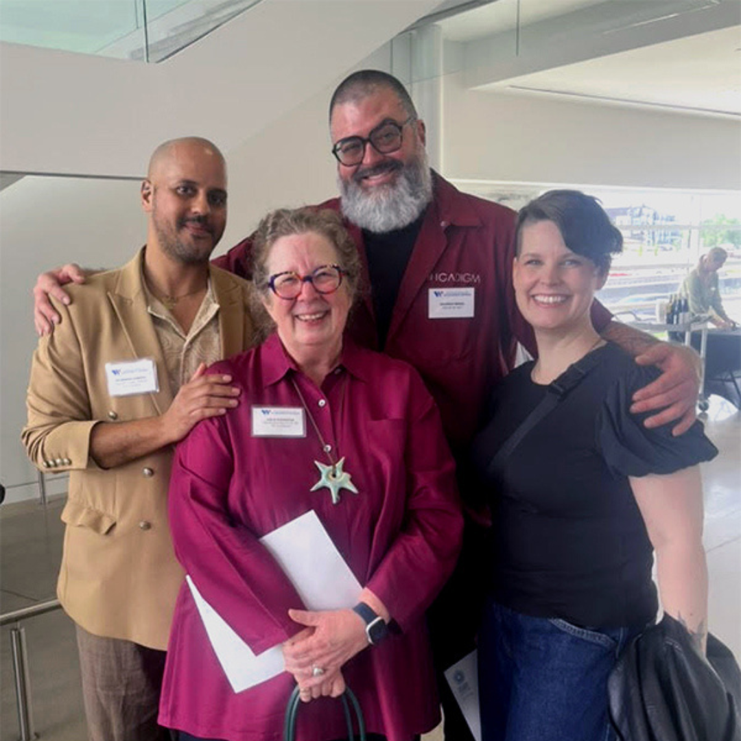 Leslie Fedorchuk, CK Ledsema, Brandon and Angela Minga stand together smiling inside a building, two with arms around the group; one holds a small green handbag and a folded program.
