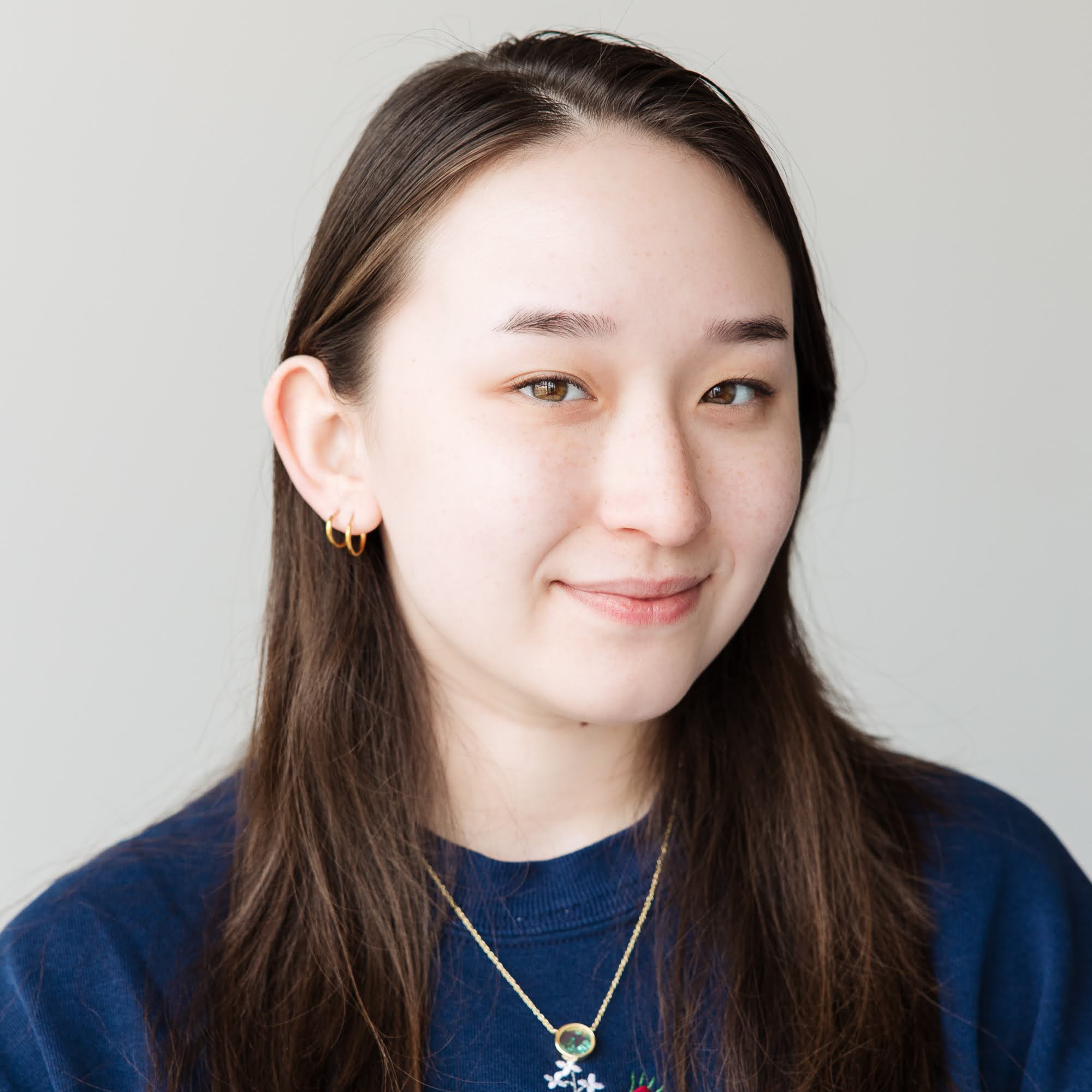 Headshot of Emily Camp smiling with a blue sweater embroidered with roses.