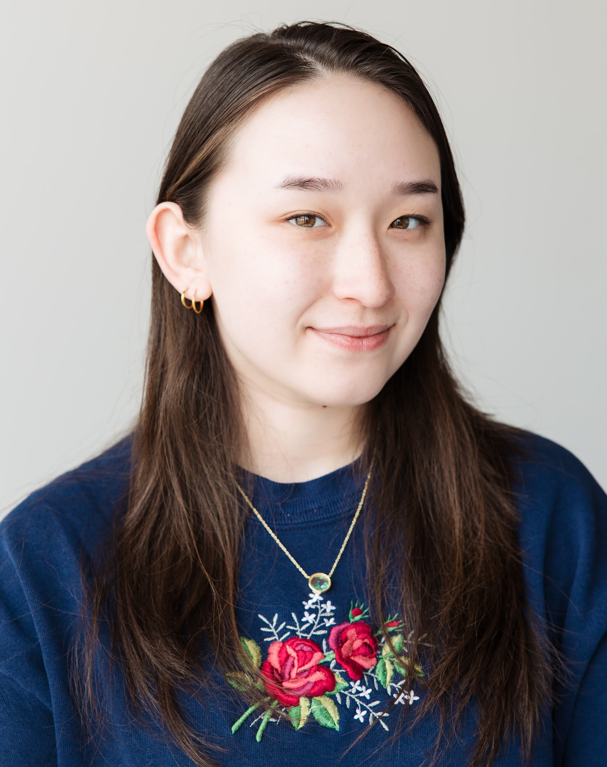 Headshot of Emily Camp smiling with a blue sweater embroidered with roses.