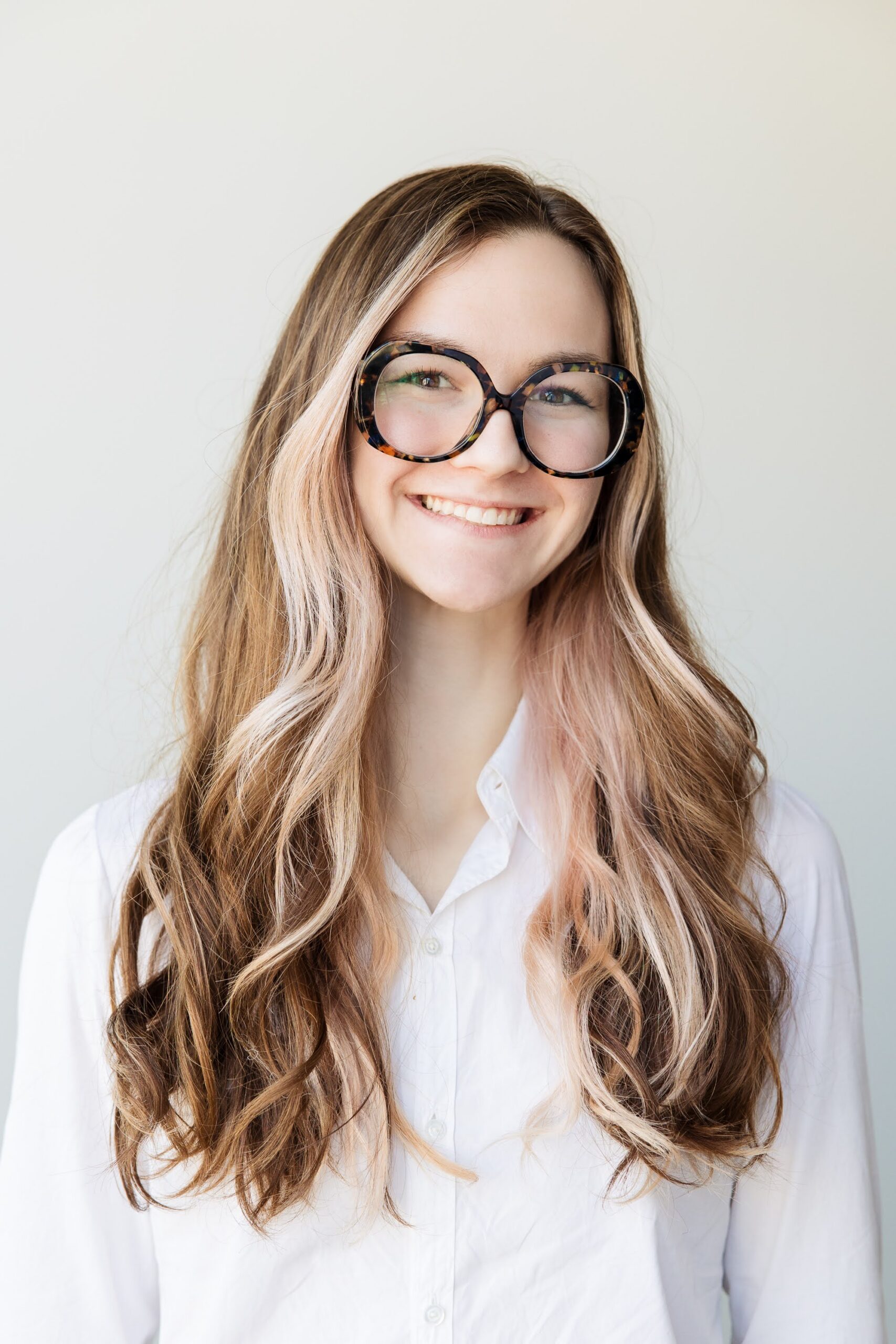 Kaitlyn Powers headshot of her smiling with large black framed glasses.