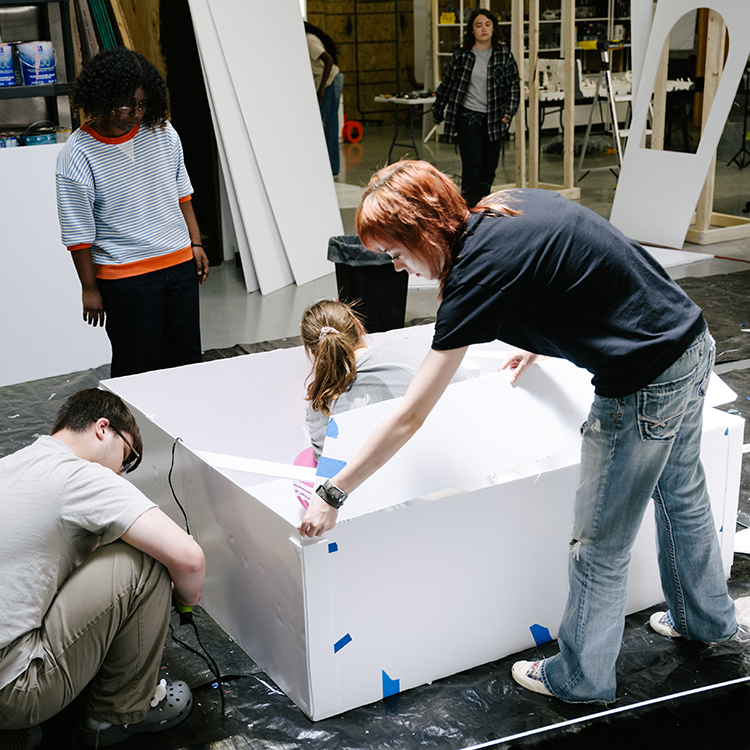 Several students collaborate on constructing a large white model or prototype in a maker space.