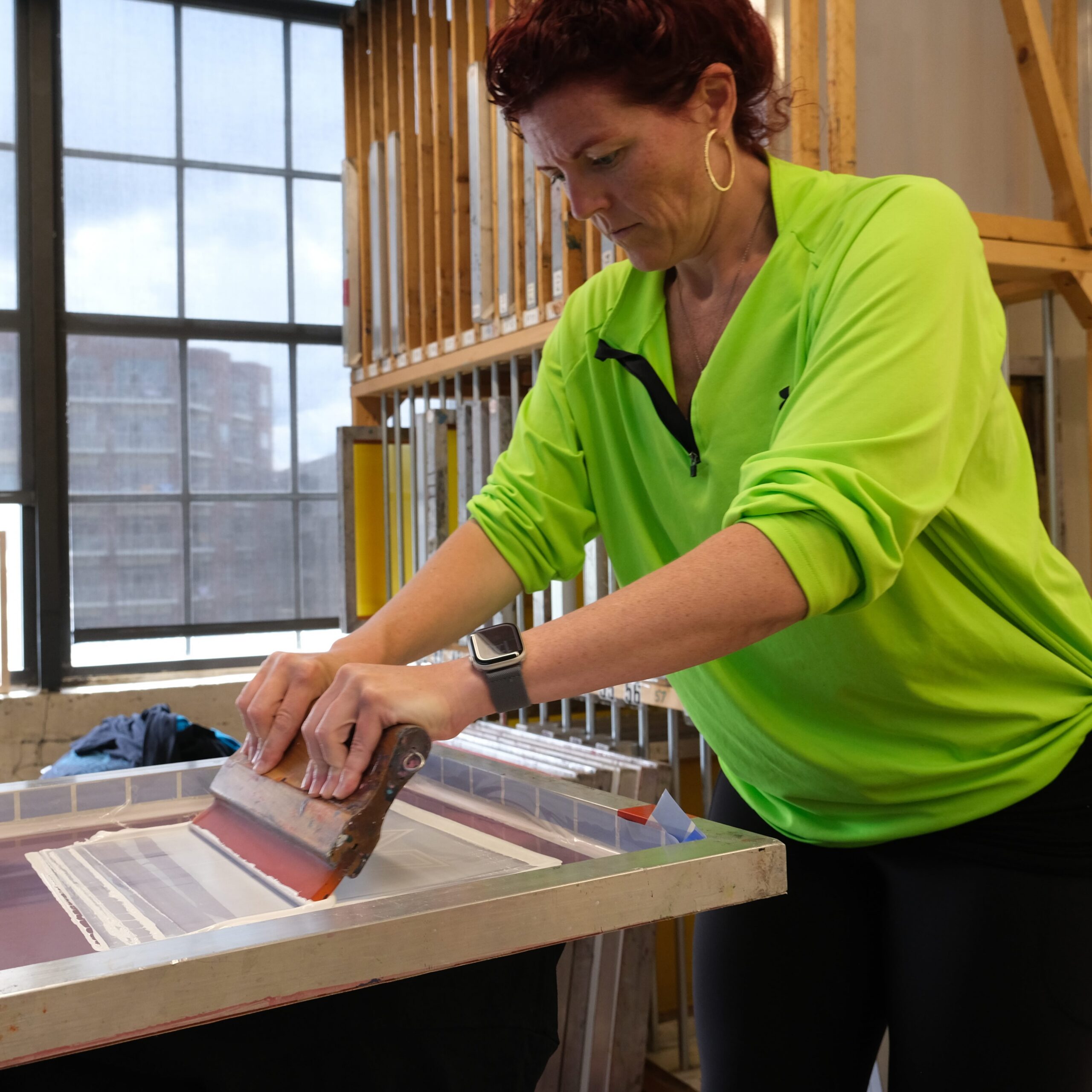 Kelly Wendel standing at a screen-printing station in a spacious printmaking studio.
