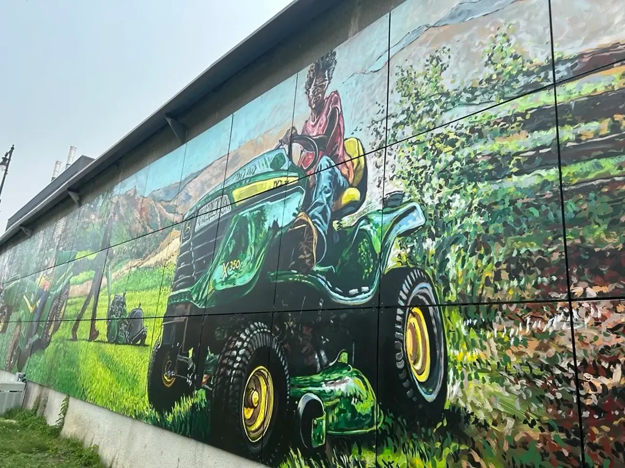 Close-up view of a mural showing a person operating a green riding lawn mower in a landscaped outdoor setting.