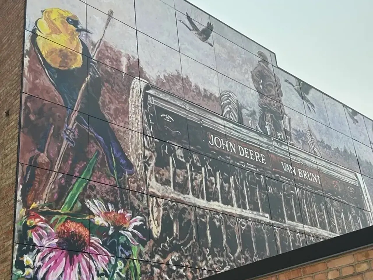 Mural panel featuring a yellow bird, wildflowers, and a historic John Deere Van Brunt agricultural seed drill.