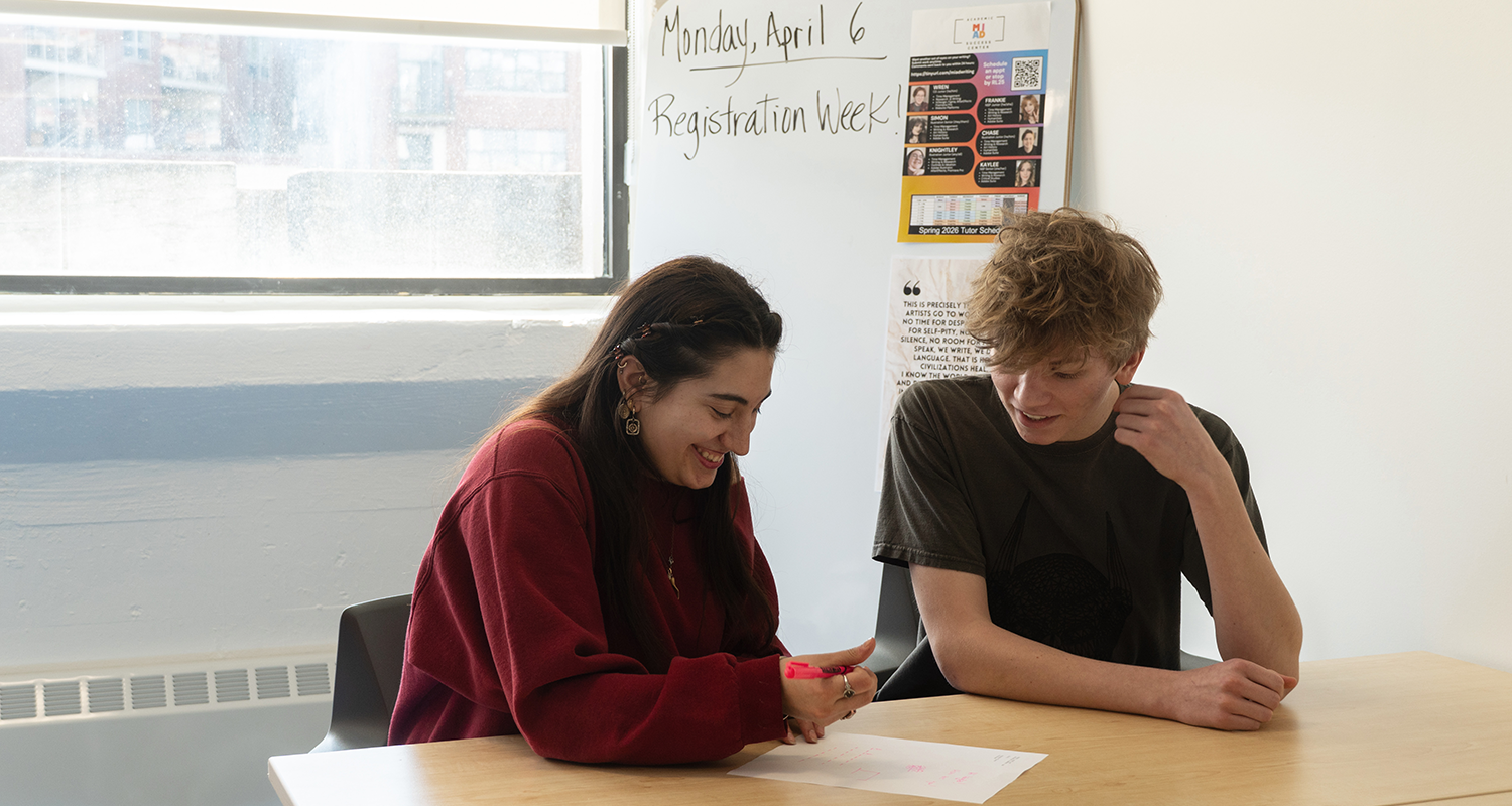 Two students seated at a table reviewing notes together in a classroom or academic support center.