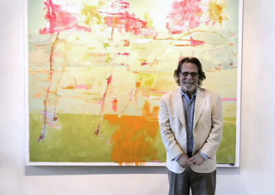 A person stands in front of a large abstract painting displayed on a gallery wall. The artwork features soft green, yellow, orange, and pink tones, with the text “TERRENCE COFFMAN” visible above it.
