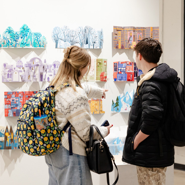 two young people look at art displayed on a gallery wall