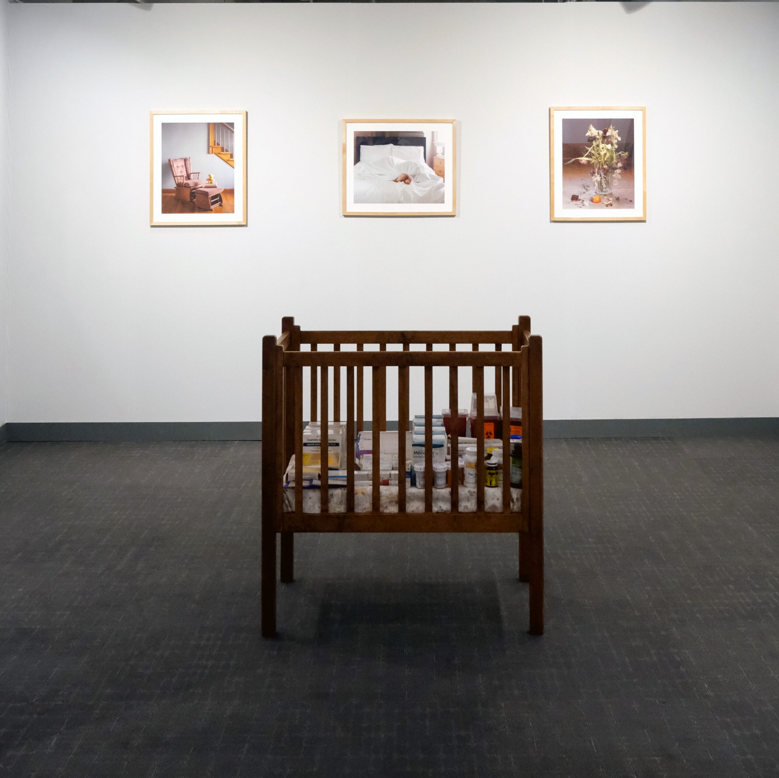 A crib filled with medication boxes with three images hanging on a wall behind it.